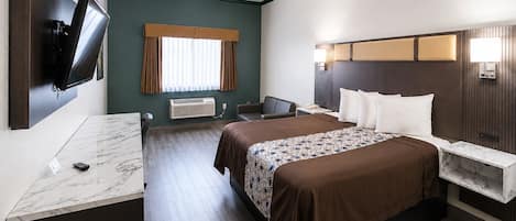 Ett hotellrum med en säng, sängbord, ett skrivbord, en platt-TV som är monterad på väggen, ett fönster med gardiner och en väggmonterad luftkonditioneringsanläggning.