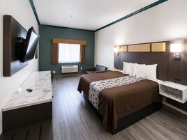 Habitación de hotel con cama, mesitas de noche, escritorio, televisor de pantalla plana en la pared, ventana con cortinas y aire acondicionado instalado en la pared.