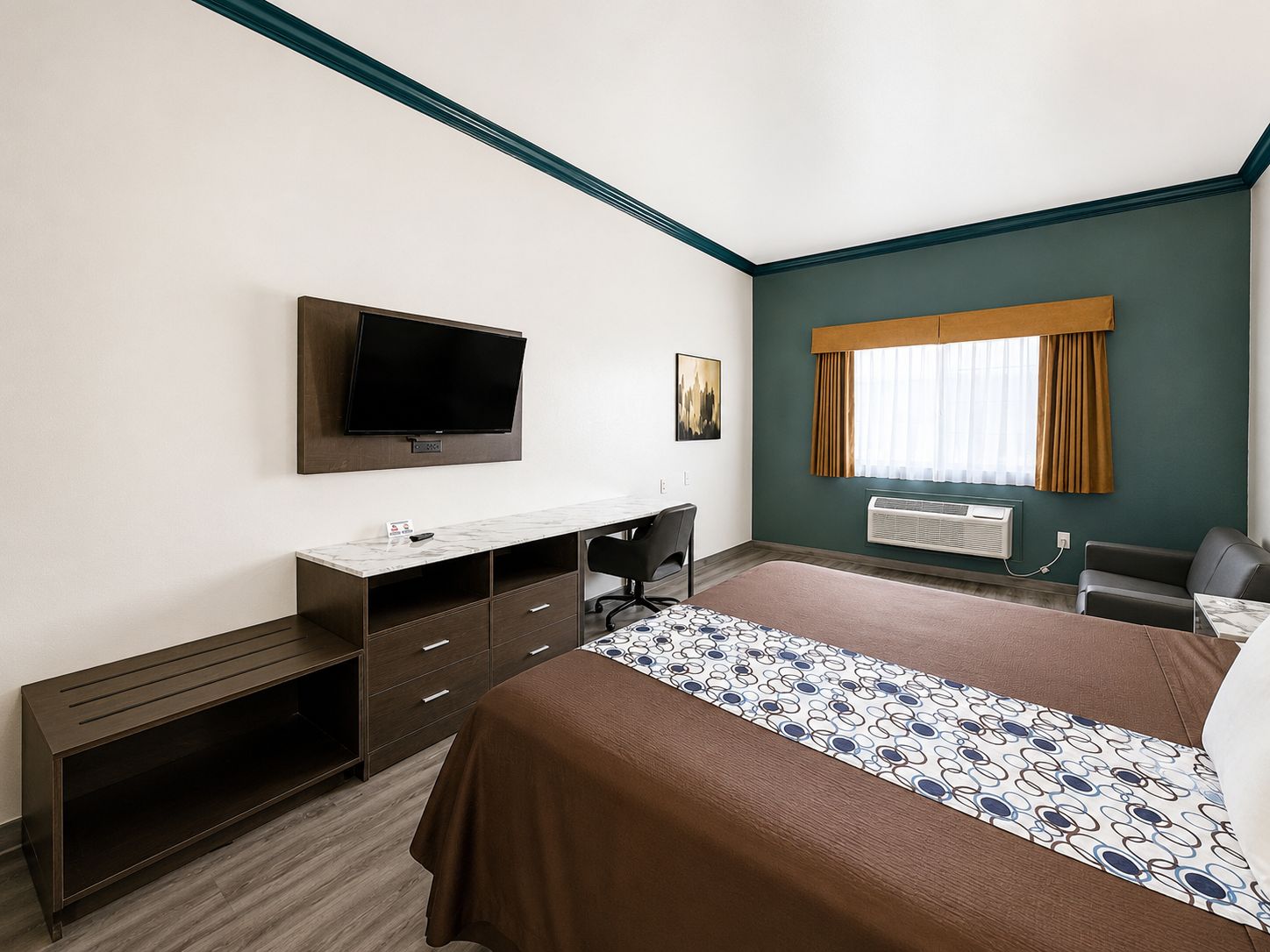 A hotel room with a bed, a desk, a television, a window with curtains, and an air conditioning unit.