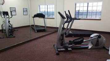Un gimnasio con equipo de cardio, cinta de correr y un espejo grande.