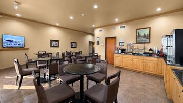 A hotel room with a dining area, a kitchen, and a TV displaying an airplane.