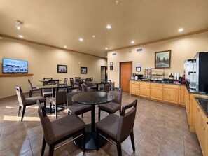 A hotel room with a dining area, a kitchen, and a TV displaying an airplane.