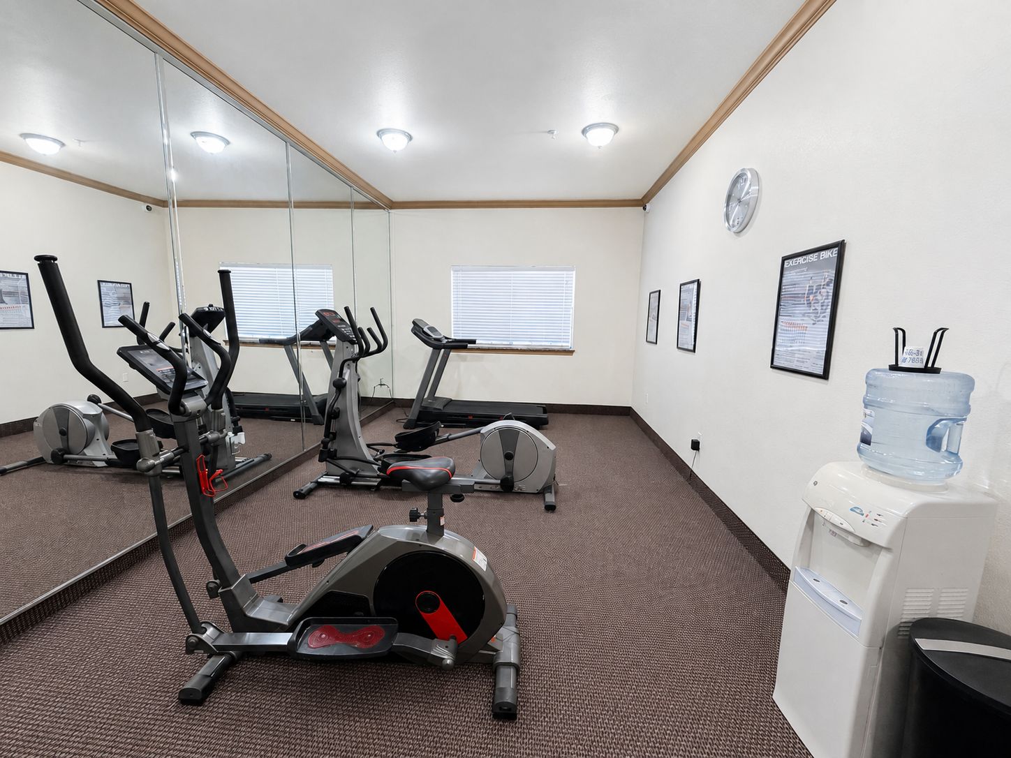A fitness room with cardio machines, a water dispenser, and exercise posters on the wall.