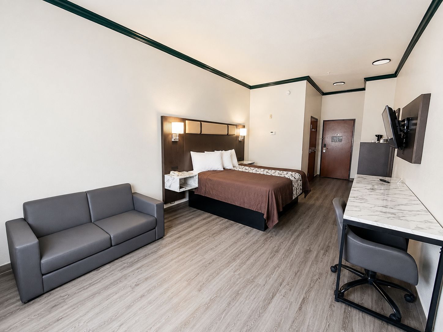 A hotel room with a bed, a desk with a chair, a sofa, and a TV mounted on the wall.