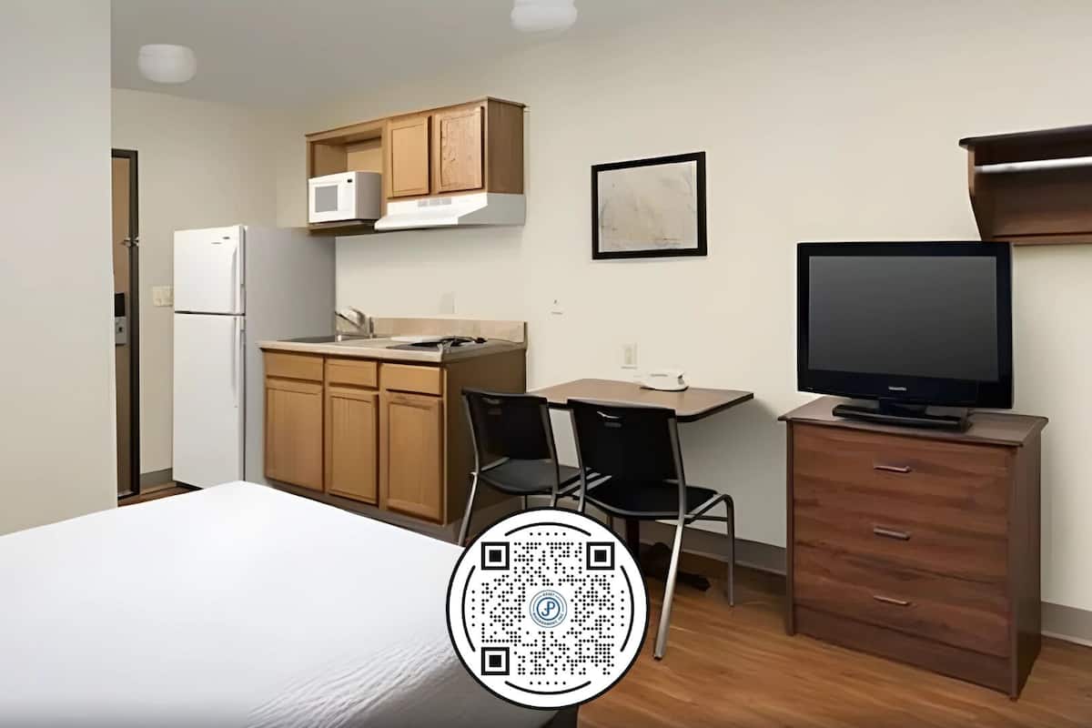A compact room with a bed, a kitchenette with a microwave, a TV, and a desk.