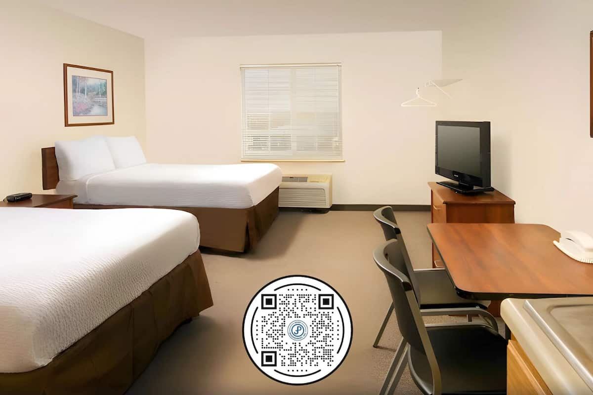 A hotel room with two beds, a desk, a television, and a window with blinds.
