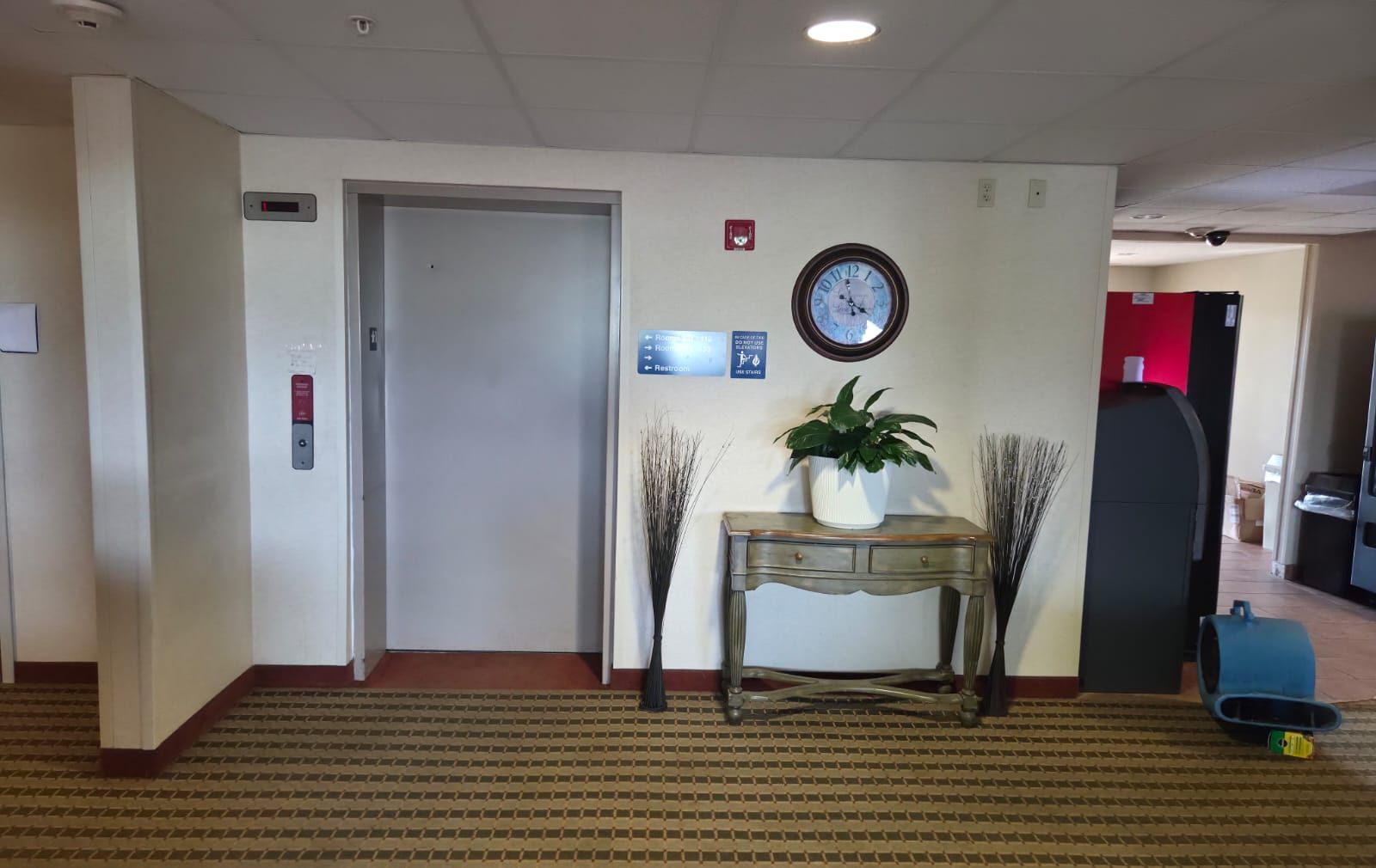 En hotellobby med en receptionsdisk, en klocka, en krukväxt och en röd vägg.
