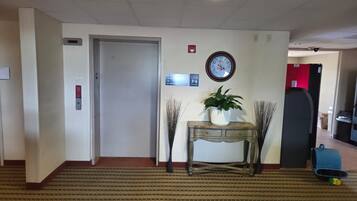 En hotellobby med en receptionsdisk, en klocka, en krukväxt och en röd vägg.