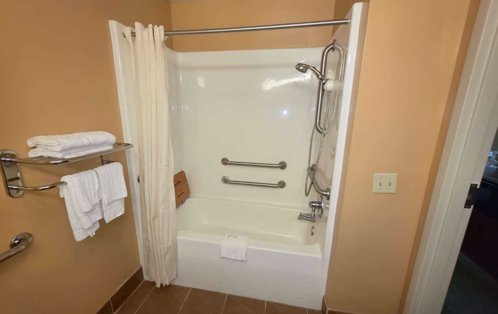 Un baño con bañera, ducha y barras de apoyo. Hay toallas en un perchero y una cortina.