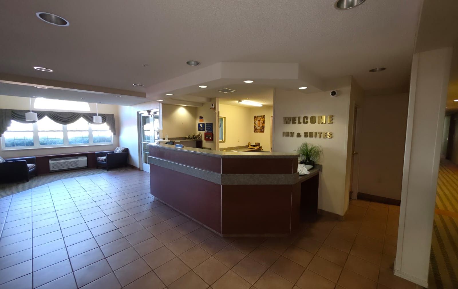 A hotel reception area with a reception desk, a seating area with sofas, and a large window providing a view.
