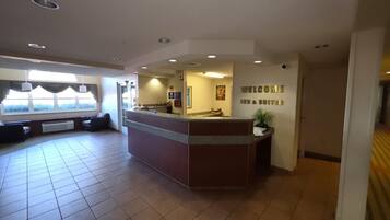 A hotel reception area with a reception desk, a seating area with sofas, and a large window providing a view.