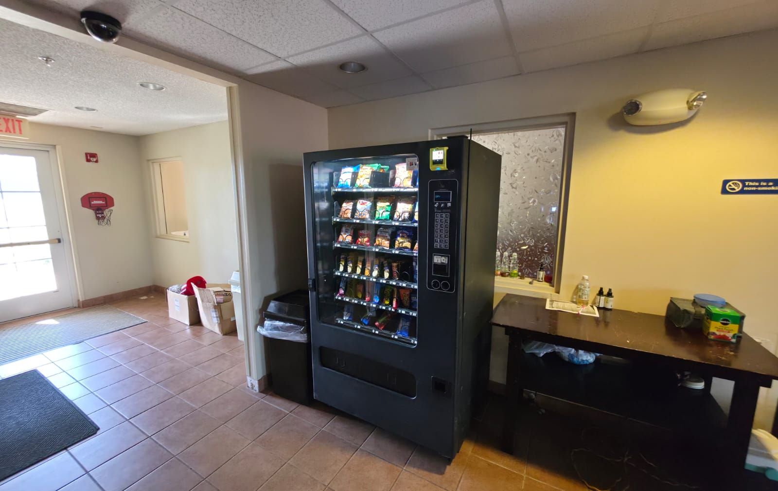 A vending machine stocked with snacks and beverages, a trash bin, and a reception desk with a computer.