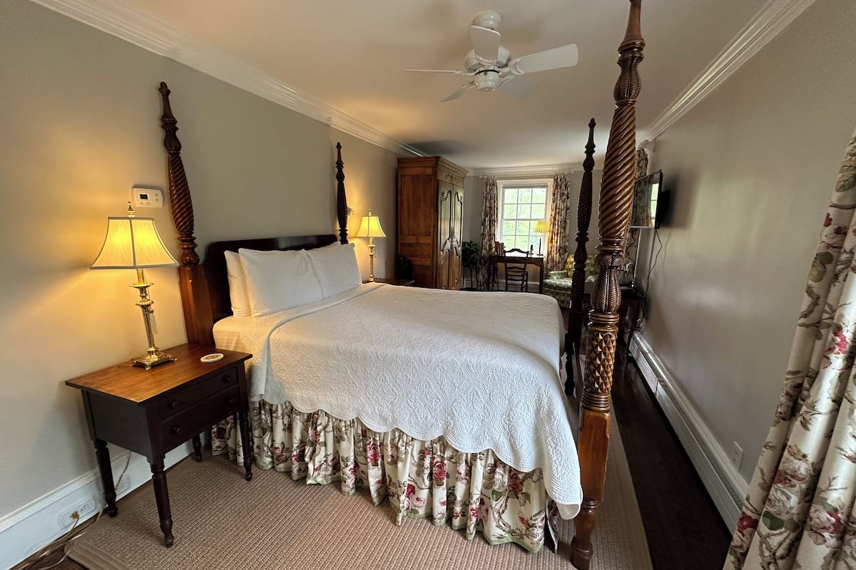 A neatly made bed with a wooden headboard, a bedside table with a lamp, and a window with curtains.