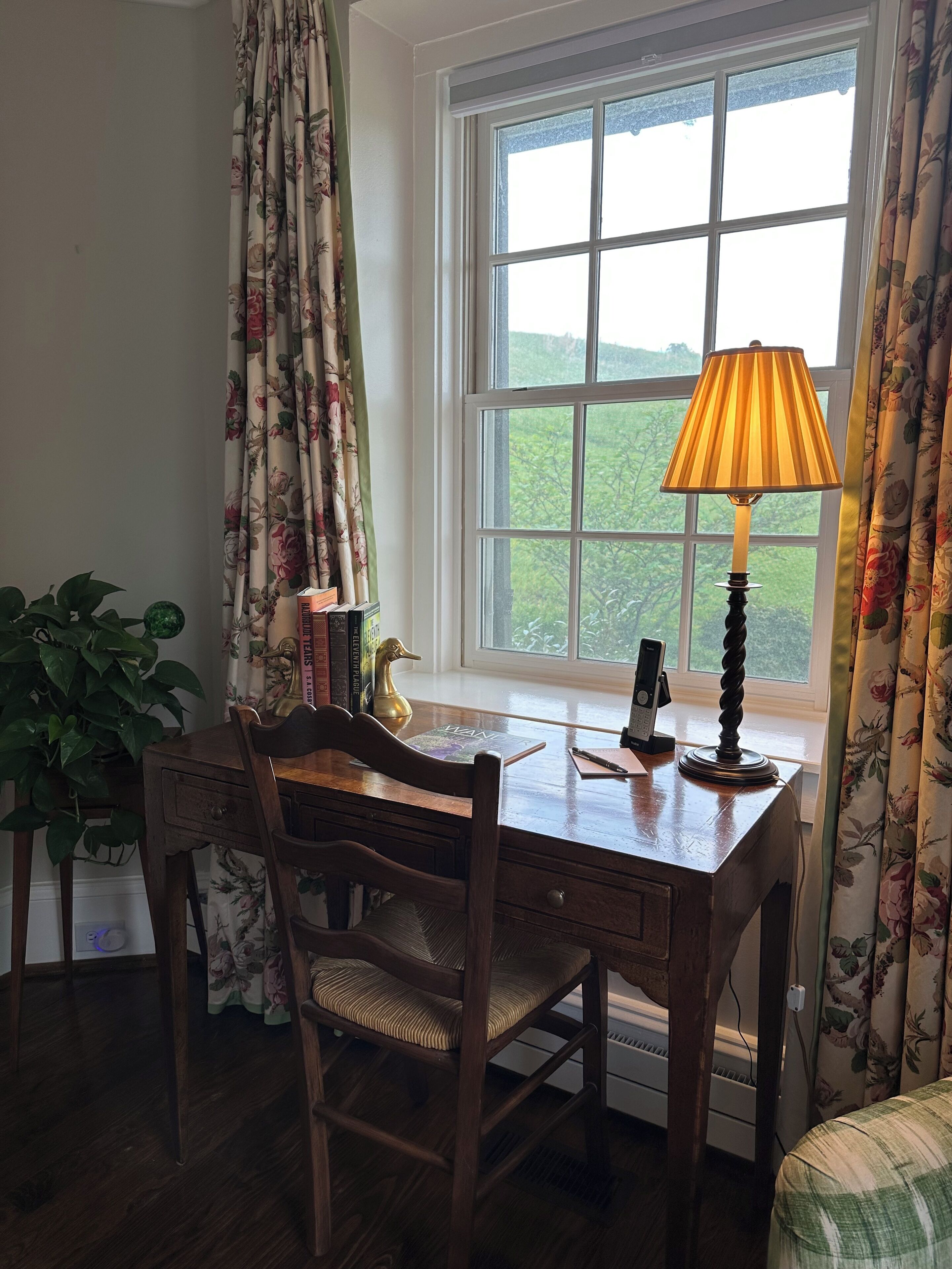 Een houten bureau met een lamp, een stoel en een raam met gordijnen.