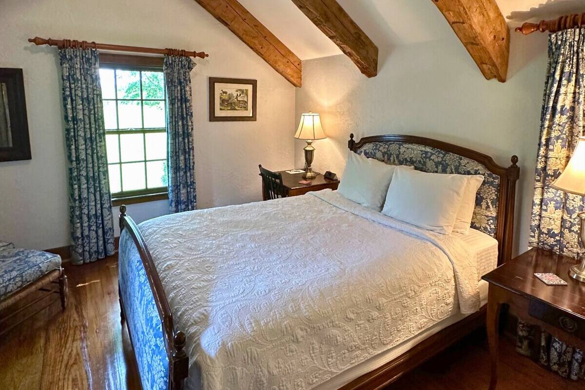 A bedroom with a large bed, wooden headboard, a bedside table with a lamp, and a window with curtains.