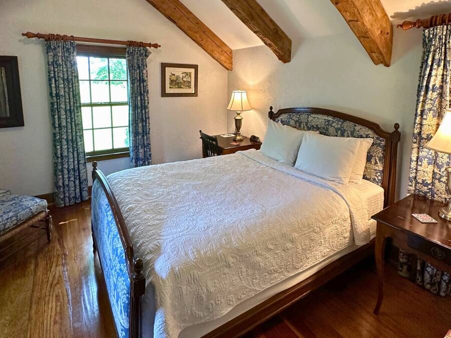 A bedroom with a large bed, wooden headboard, a bedside table with a lamp, and a window with curtains.
