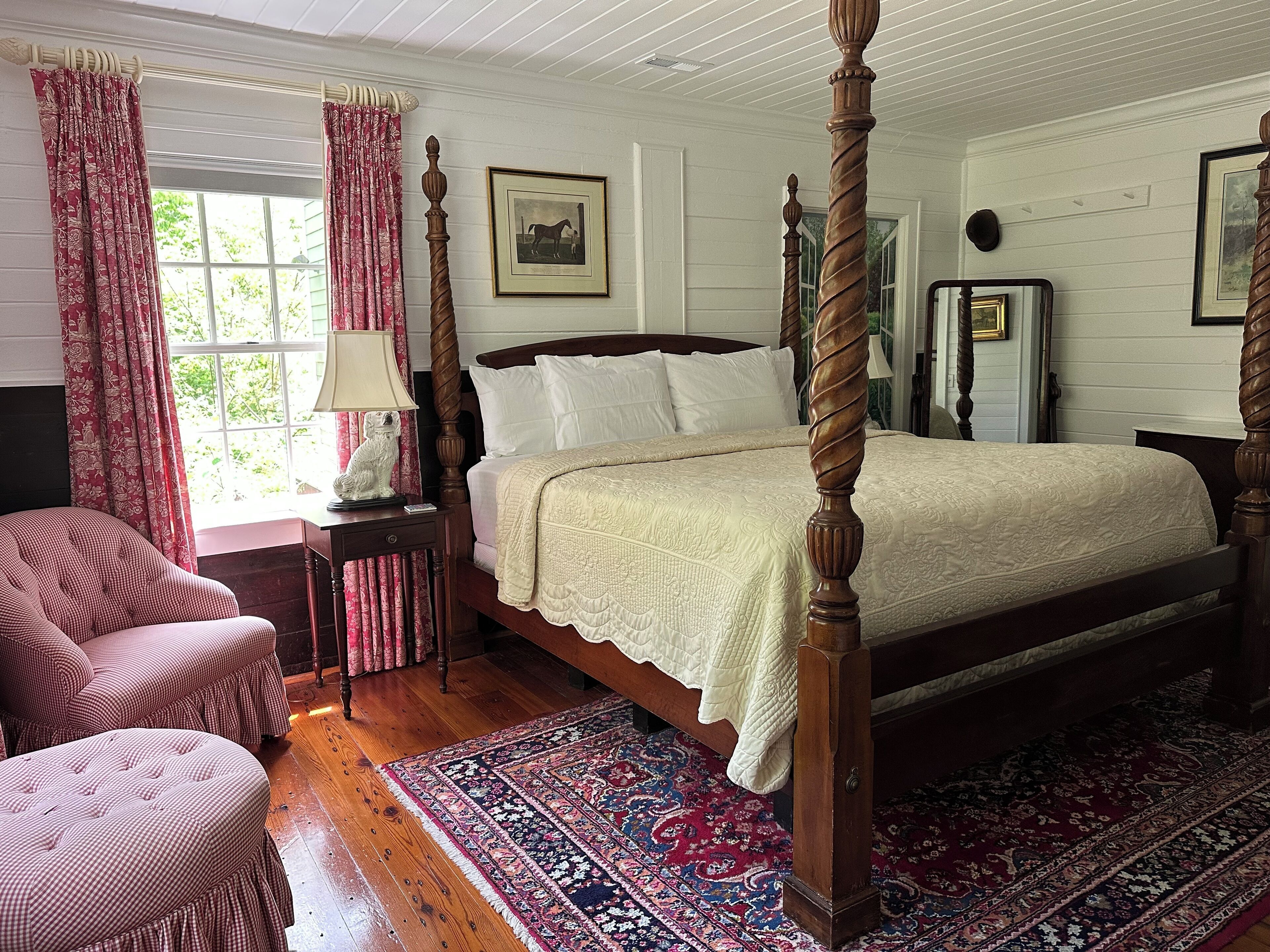 Ein Bett mit Baldachin, mit weißer Bettdecke, einem Teppich in Rot-Weiß-Muster und einem Holzboden.