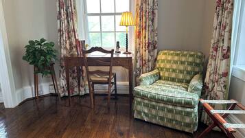 Una habitación con un escritorio de madera, un sillón verde a cuadros, una planta en maceta y una ventana con cortinas estampadas de flores.