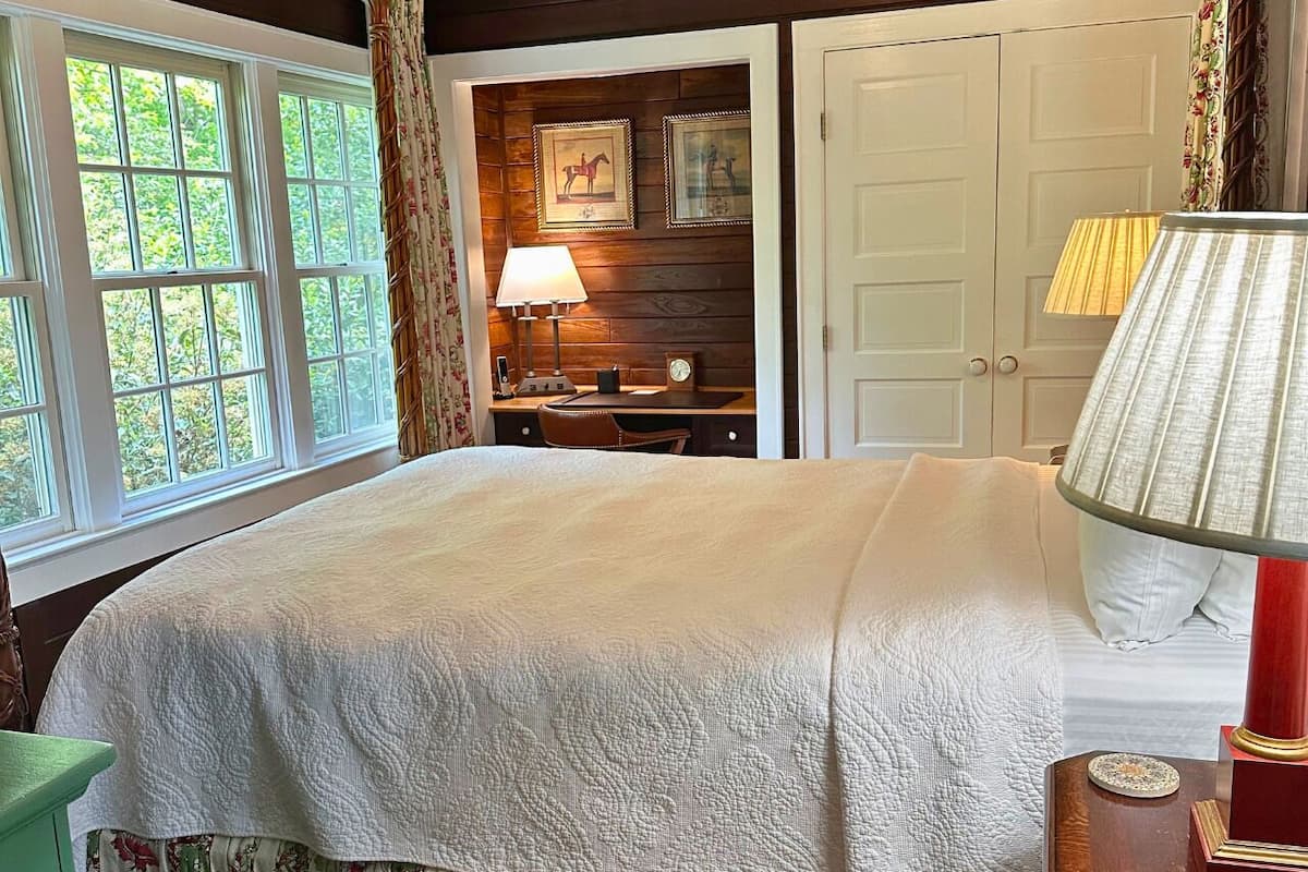 A bedroom with a large bed, a nightstand with a lamp, a dresser, and a door.