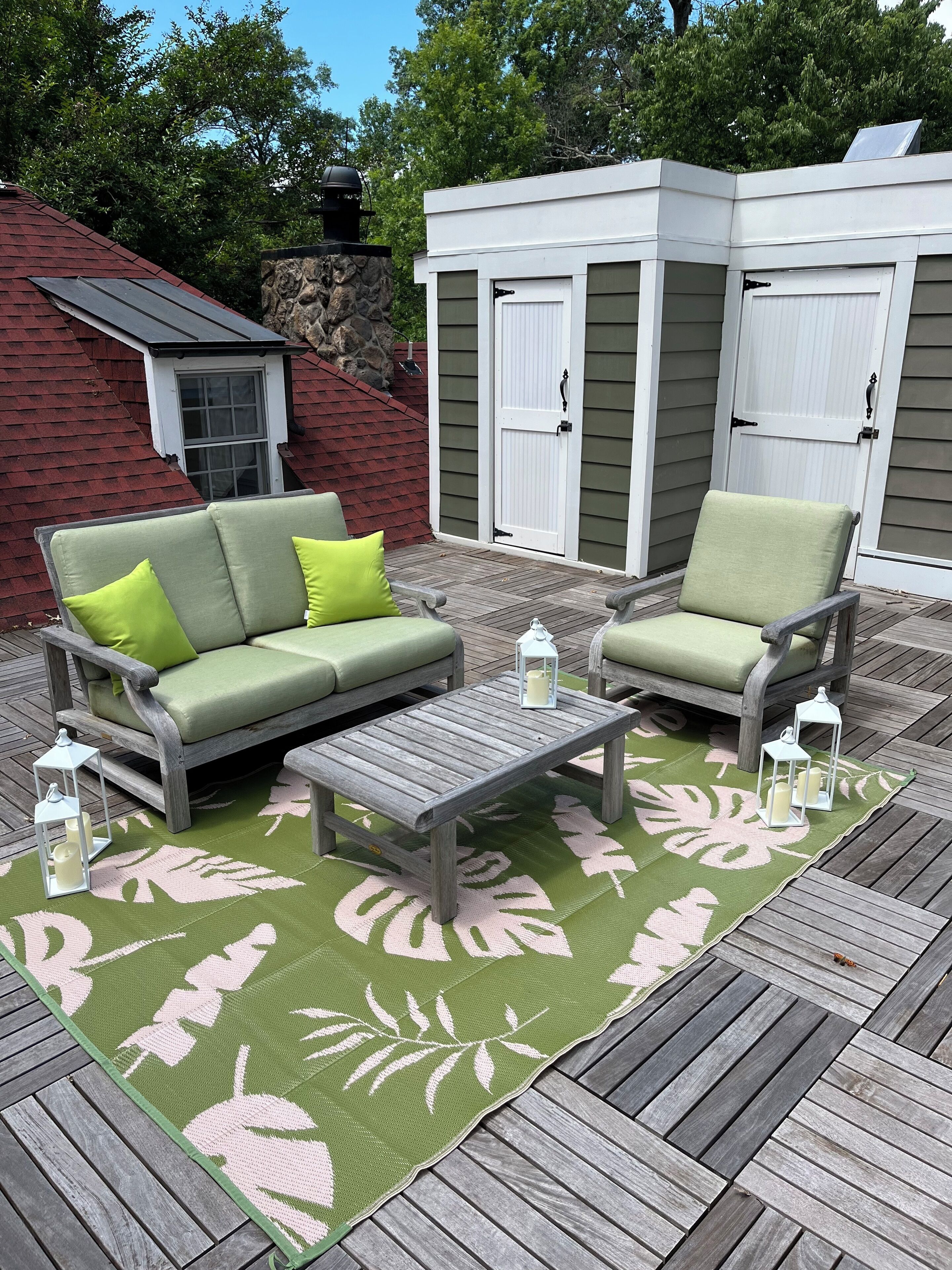 Une terrasse dotée d’un tapis à motifs verts et roses, d’une table basse en bois et de deux fauteuils verts avec des coussins.