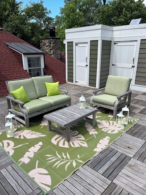 A deck with a green and pink patterned rug, a wooden coffee table, and two green cushioned chairs.