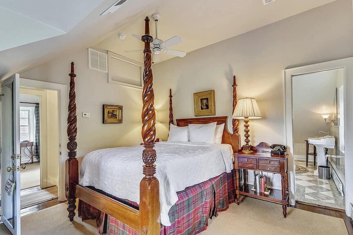 A four-poster bed with a wooden headboard, a bedside table with a lamp, and a mirror.