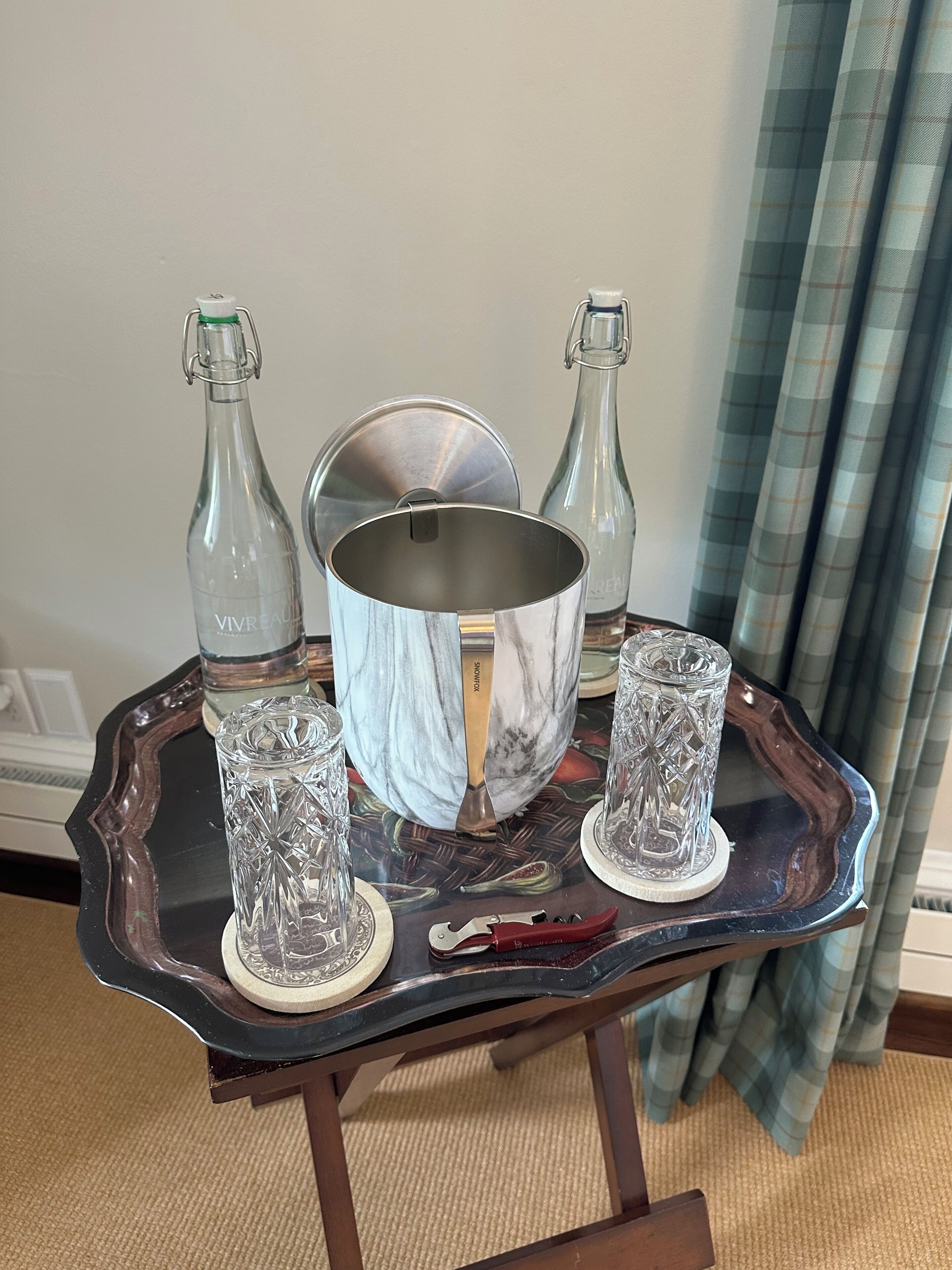 Ein Tablett mit einer Metallschüssel, zwei Glasflaschen und zwei Kristallgläsern auf einer Tischplatte.