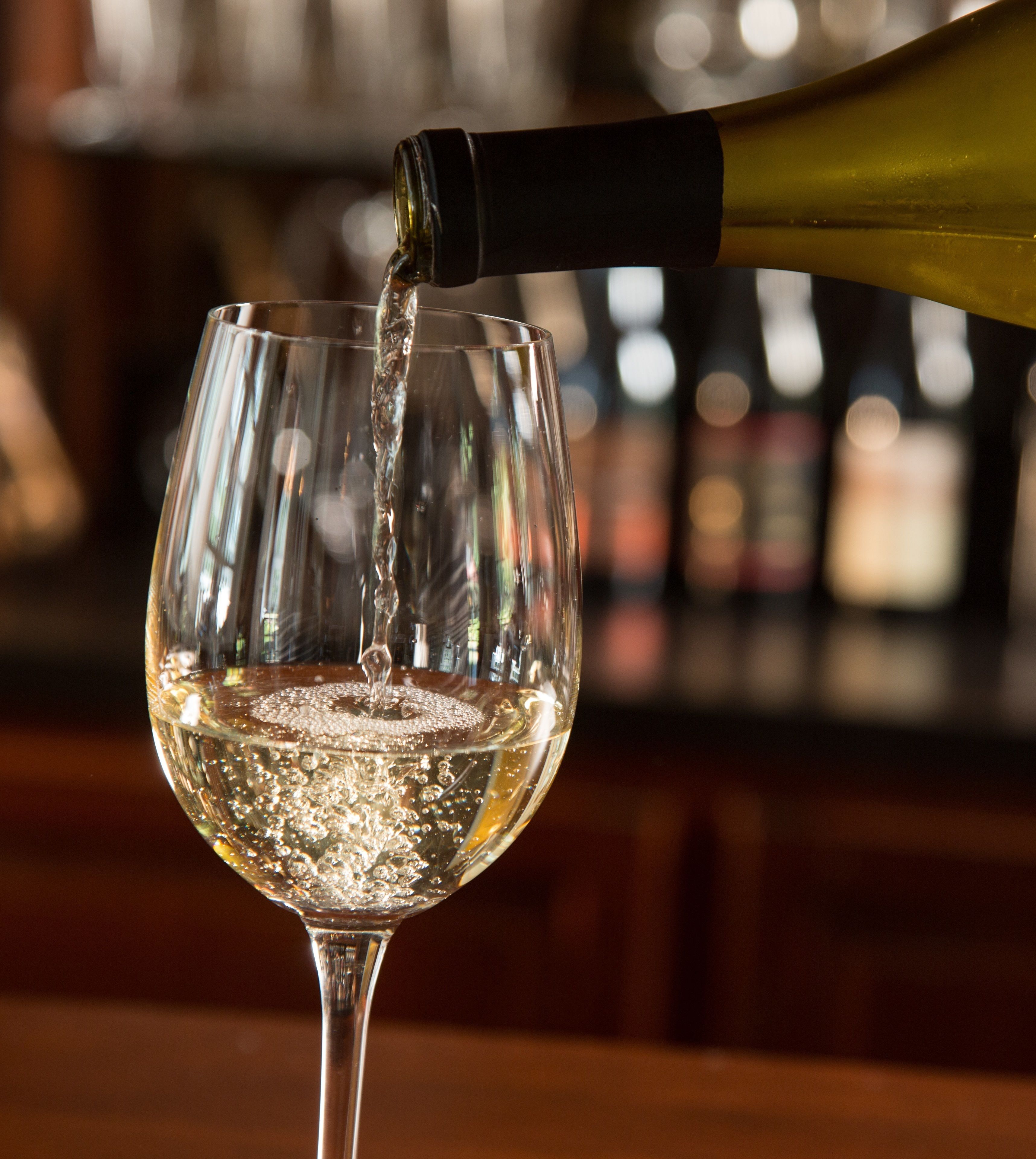 A glass being filled with a clear liquid, likely wine, from a bottle.