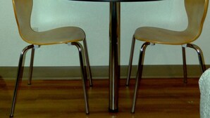 Un coin repas avec une table ronde, deux chaises et un téléviseur à écran plat fixé au mur.