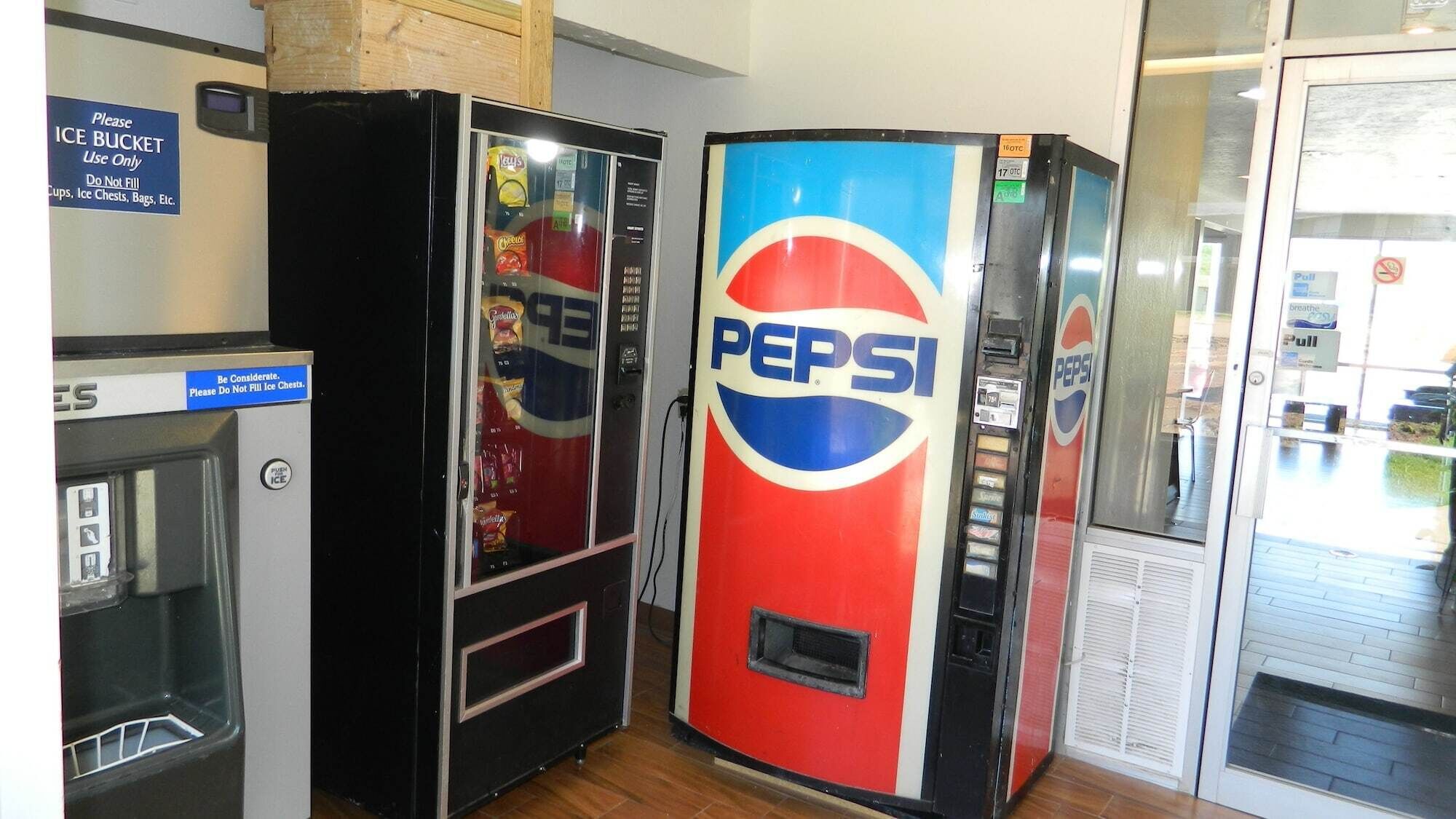 A row of vending machines, including a Pepsi cooler and a smaller ice cooler, in a commercial setting.