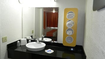 Un baño de hotel con un lavamanos blanco, encimera negra y un espejo con un sujetapapeles amarillo.