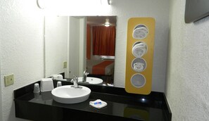 Une salle de bain d’hôtel avec un lavabo blanc, un plan de toilette noir et un miroir doté d’un porte-serviette jaune.