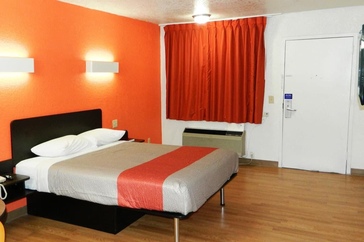 Una habitación de hotel con una cama, un escritorio con teléfono, una cortina roja y una puerta blanca.
