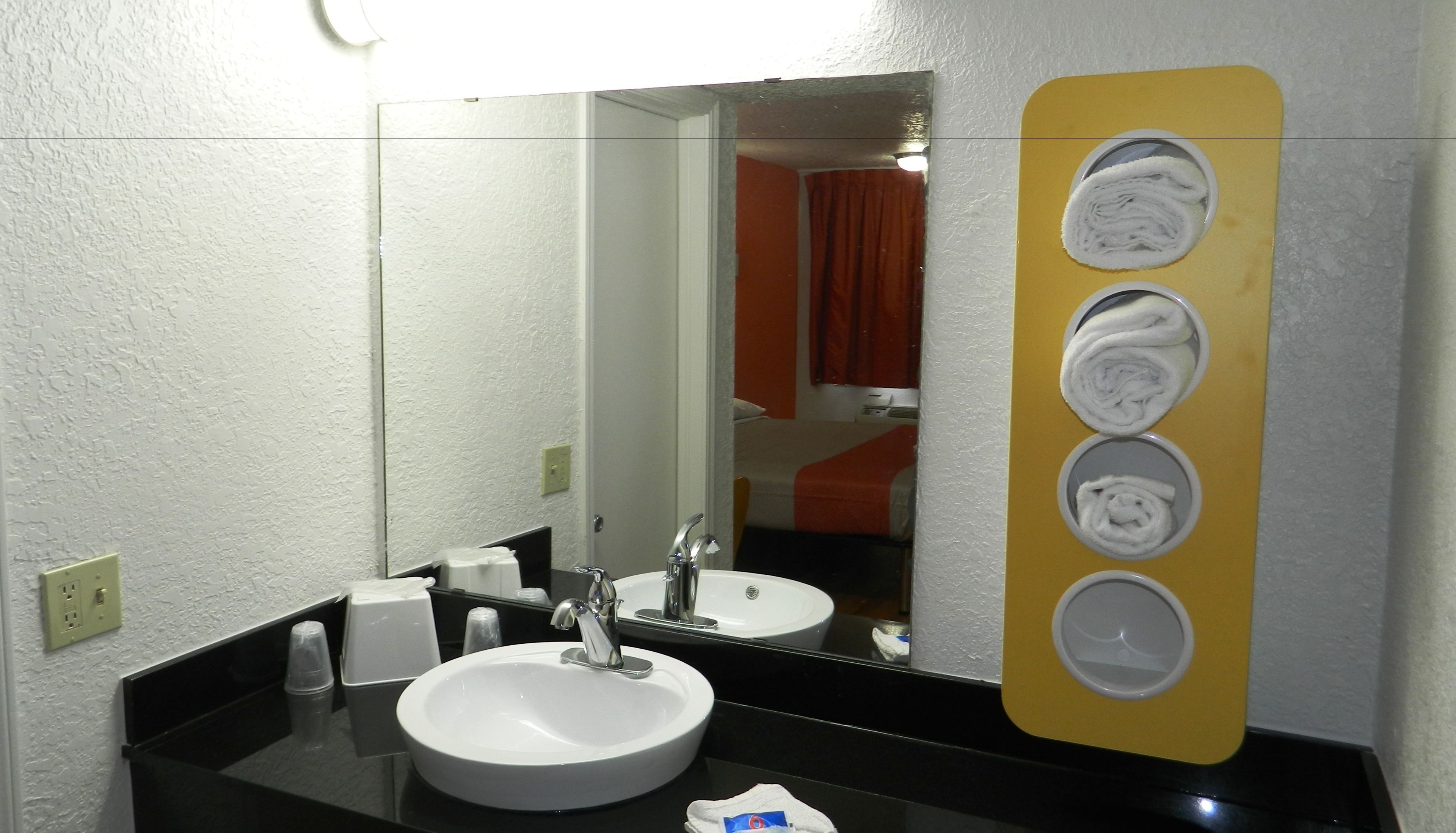 A bathroom with a sink, mirror, and towel dispenser.