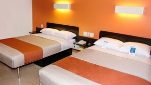 Une chambre d’hôtel avec deux lits, chacun agrémenté d’un oreiller blanc et d’un élément décoratif marron. Des appliques murales sont fixées au-dessus des lits, et une table de chevet est placée à côté de chaque lit, avec un téléphone et un petit objet.