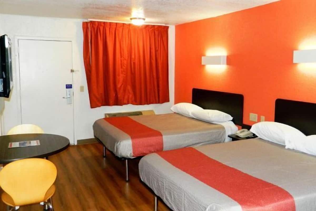 Habitación de hotel con dos camas, una mesita, una silla y una cortina roja.