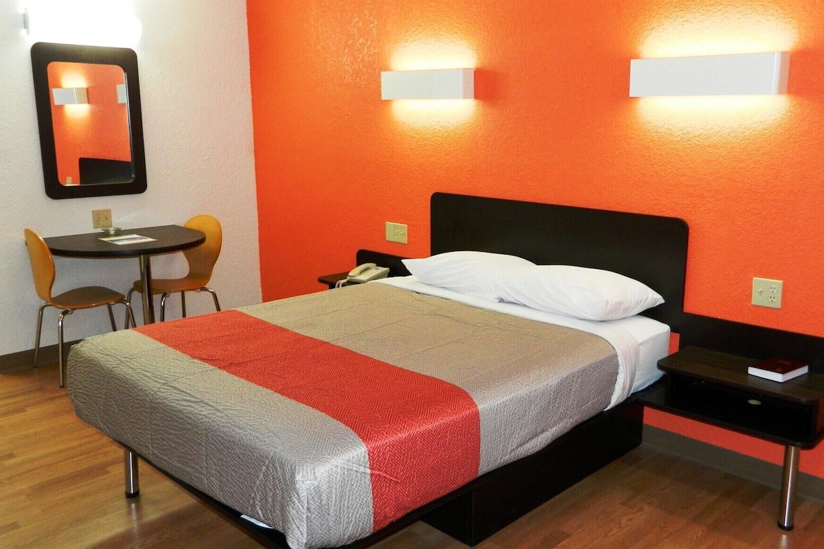 Una habitación de hotel con una cama, un escritorio, dos sillas y una mesita de noche.