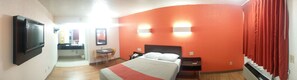 Une chambre d’hôtel comprenant un lit, des tables de chevet, un bureau, une chaise, une télévision et une salle de bain avec un miroir et un lavabo.