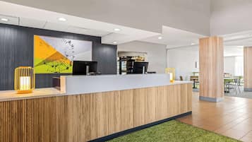 Un espace d’accueil doté d’un comptoir de réception en bois, d’un grand tableau abstrait et d’un aménagement intérieur moderne.