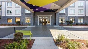 A modern building entrance with a geometric ceiling design, a central pathway, and a bench. - Spark by Hilton Port Wentworth Savannah (Port Wentworth)