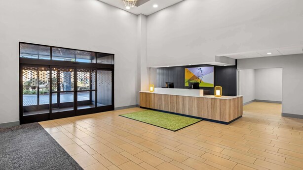 A modern reception area with a wooden reception desk, a large window with a view, and a green rug on the floor. - Spark by Hilton Port Wentworth Savannah (Port Wentworth)