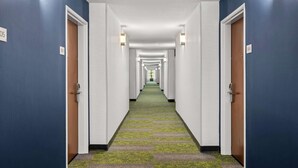 A hotel hallway with a green carpet, white walls, and doors marked with room numbers. - Spark by Hilton Port Wentworth Savannah (Port Wentworth)