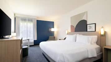 A hotel room with a bed, a desk, a chair, a TV, and a window with curtains.