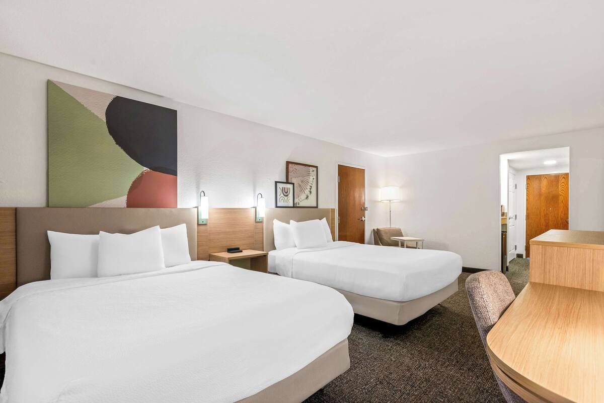 A hotel room with two beds, a desk, a chair, and a large abstract painting on the wall.