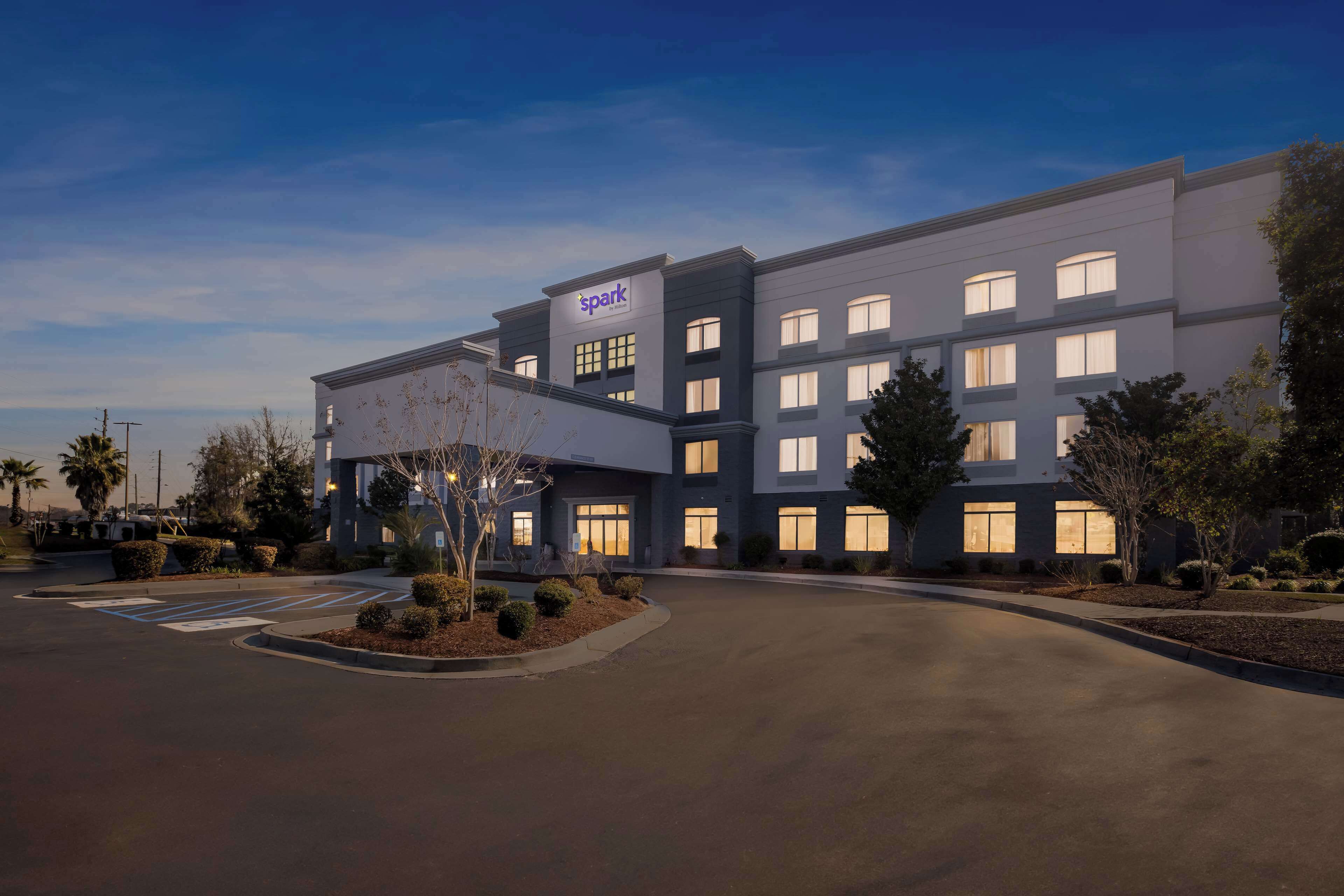 Een modern hotel met een 'spark'-bord, een parkeerplaats en aangelegde groene zones.