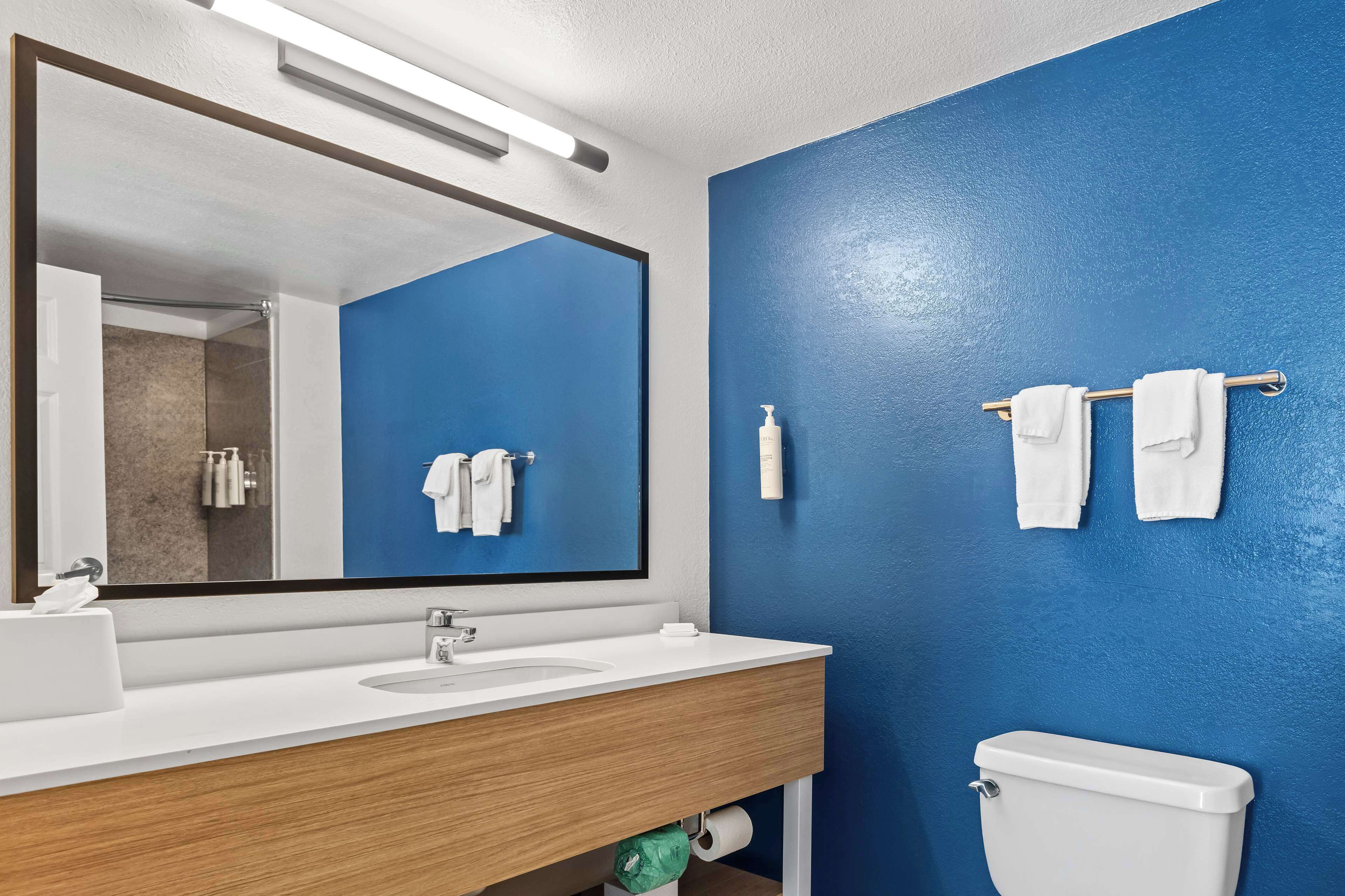 A bathroom with a blue wall, a white sink, a mirror, and a toilet.