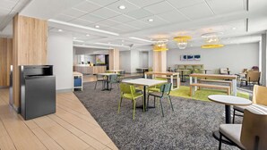 A modern dining area with tables and chairs, a small refrigerator, and a television. - Spark by Hilton Port Wentworth Savannah (Port Wentworth)