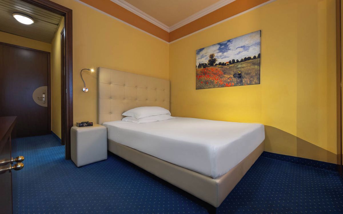 Une chambre d’hôtel avec un lit, des tables de chevet, un tableau au mur et une porte.