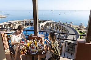 Un balcon avec une table préparée pour le petit-déjeuner, donnant sur une piscine et un port de plaisance.