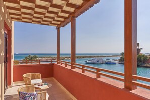 Een balkon met rieten meubilair, uitzicht op zee en boten op de achtergrond.